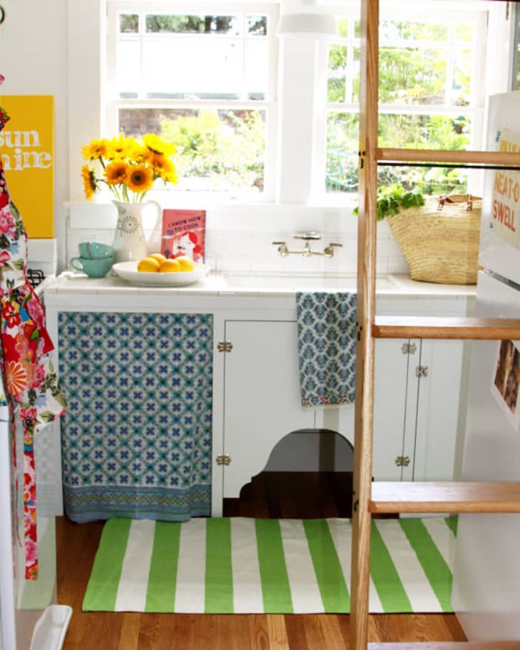 Bright kitchen with sunflowers, striped rug, colorful towels, and a basket on the counter near a window.