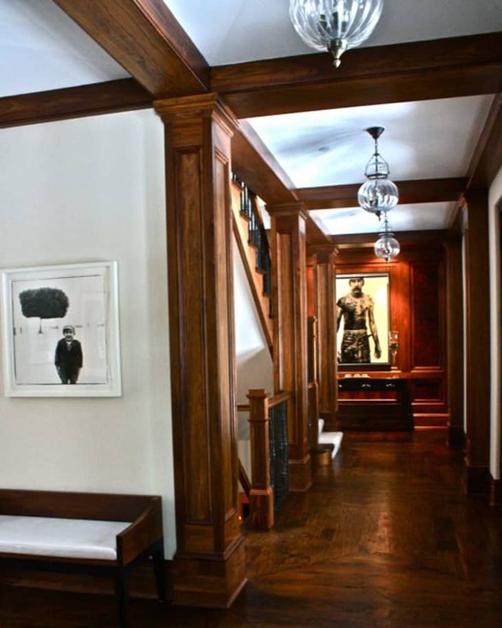Wood-paneled hallway with framed art, glass pendant lights, and a staircase.
