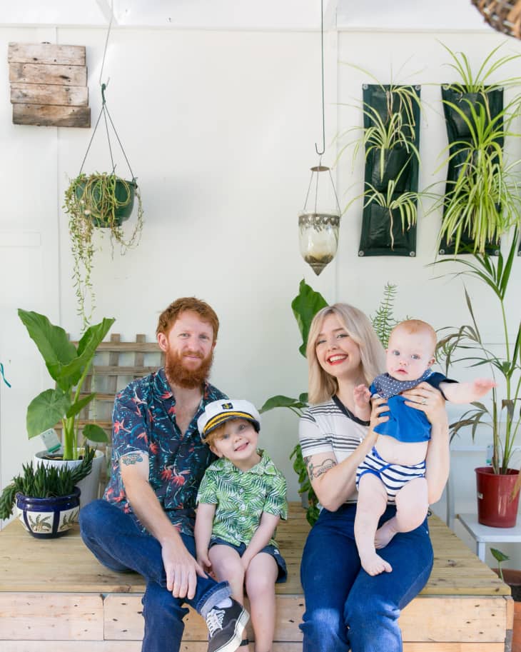 Family sitting on a wooden bench surrounded by hanging and potted plants, with two children and two adults smiling.