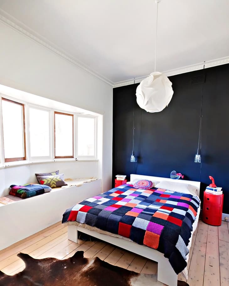 Bedroom with a colorful patchwork quilt, black accent wall, pendant lights, and a red side table.