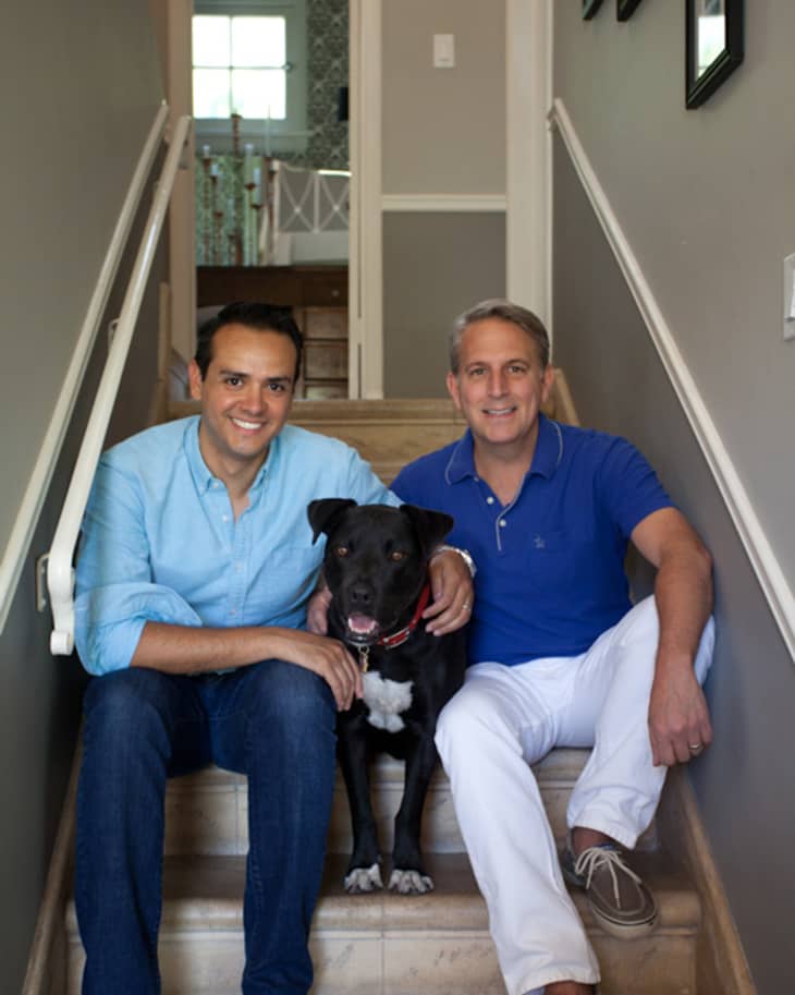 Two men sitting on stairs with a black dog, smiling at the camera.