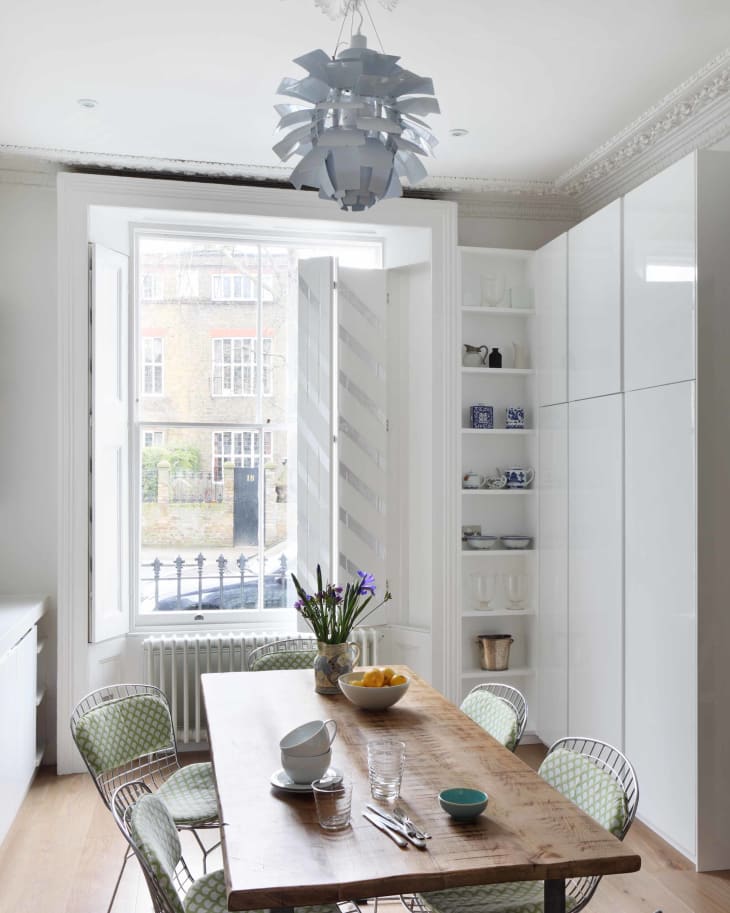 Dining room with wooden table, wire chairs, modern chandelier, and open shelves displaying dishes.