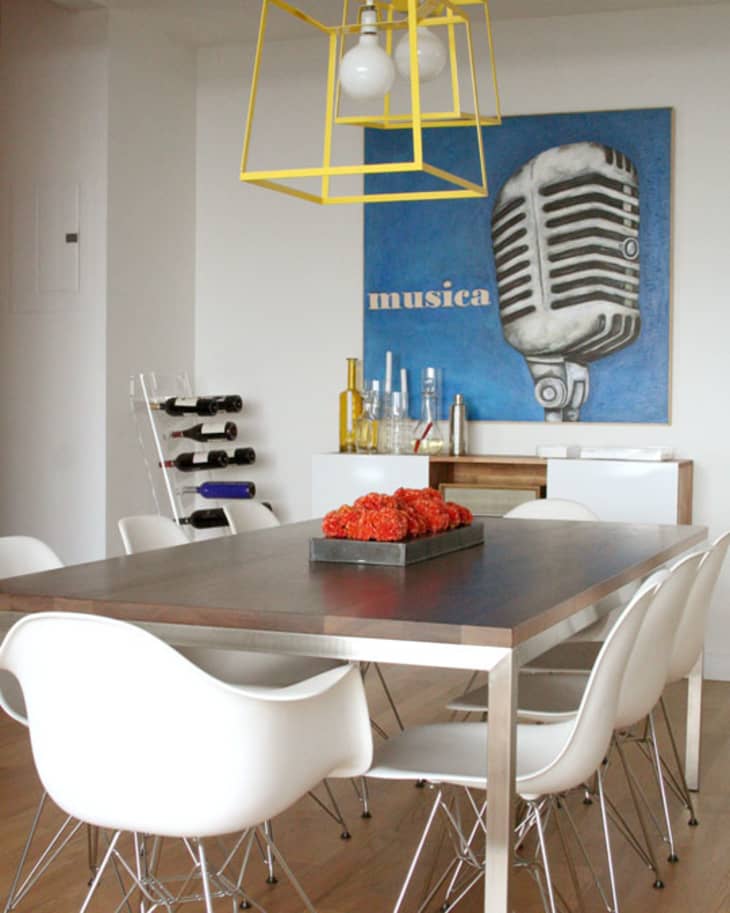 Dining room with white chairs, wooden table, yellow pendant light, and a blue artwork featuring a vintage microphone.