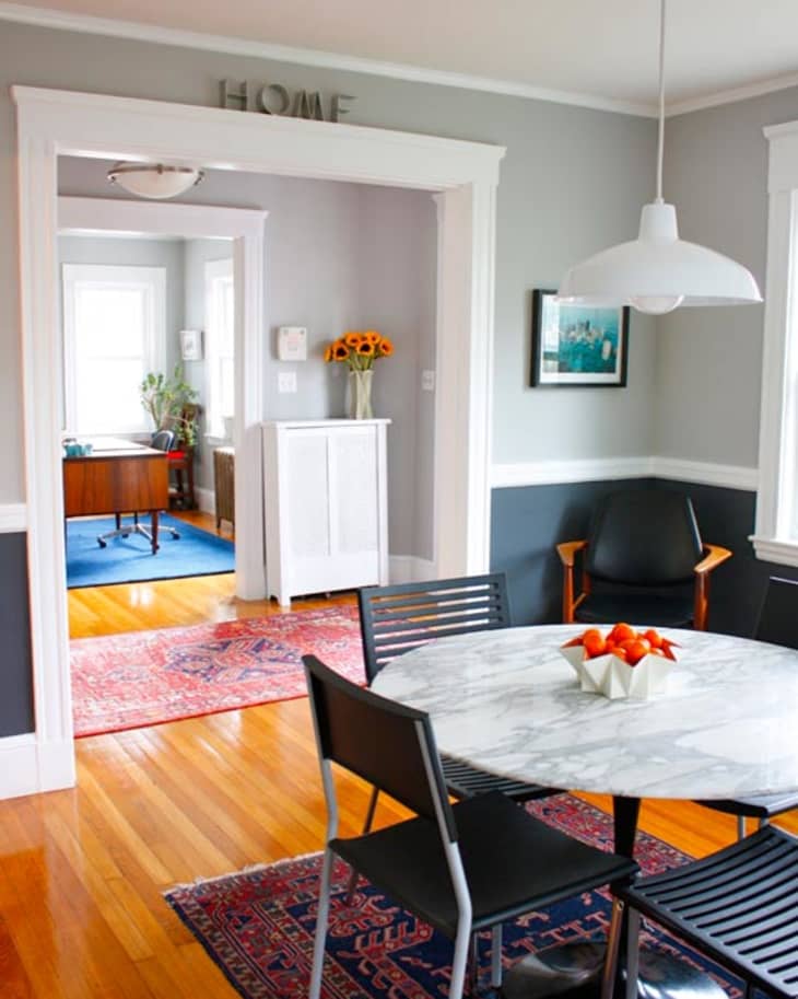 Dining room with marble table, black chairs, pendant light, and view into office with sunflowers and red rugs.