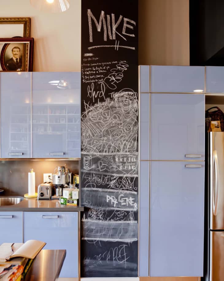 Kitchen with light blue cabinets, stainless steel appliances, and a black chalkboard wall with scribbles and "Mike" written on top.