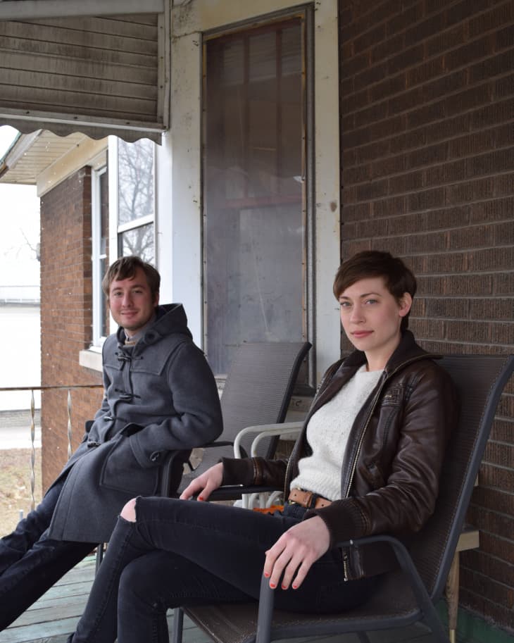 Two people sitting on a porch in chairs, one wearing a gray coat and the other in a brown leather jacket.
