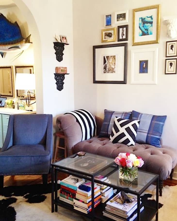 Cozy living room with a tufted sofa, blue armchair, geometric pillows, glass coffee table, and eclectic wall art.