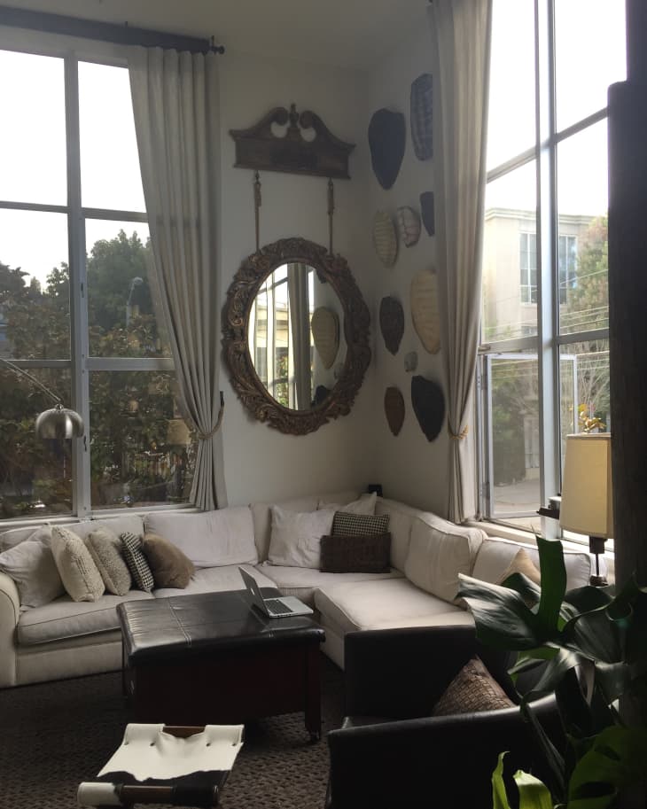 Cozy living room with a white sectional sofa, ornate mirror, wall decor, and large windows with curtains.