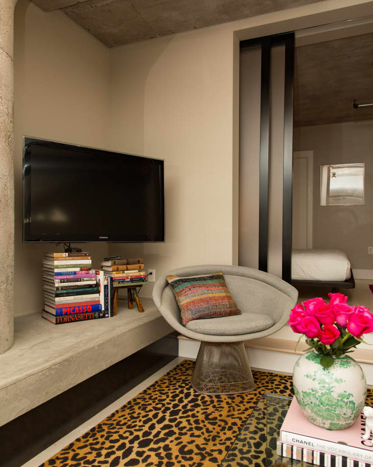 Modern living room with a TV, gray chair, leopard rug, books, and pink flowers in a vase on a glass table.