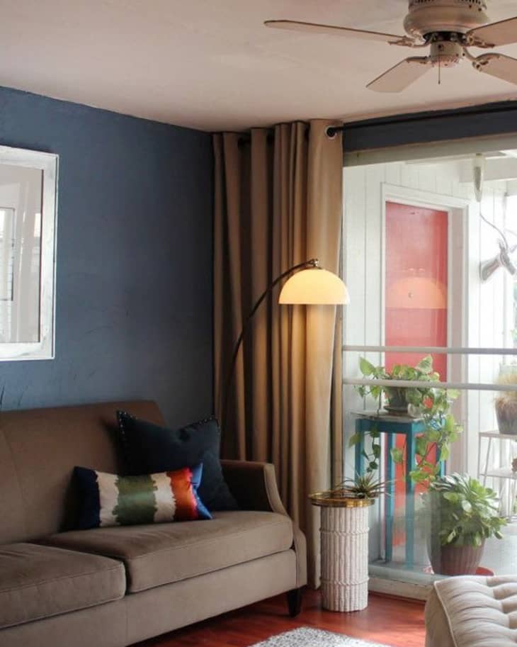 Living room with a brown sofa, colorful pillows, floor lamp, and plants by a window.