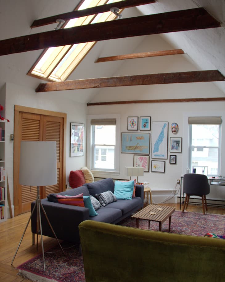 Loft living room with skylights, gray sofa, colorful cushions, wooden coffee table, and framed art on walls.