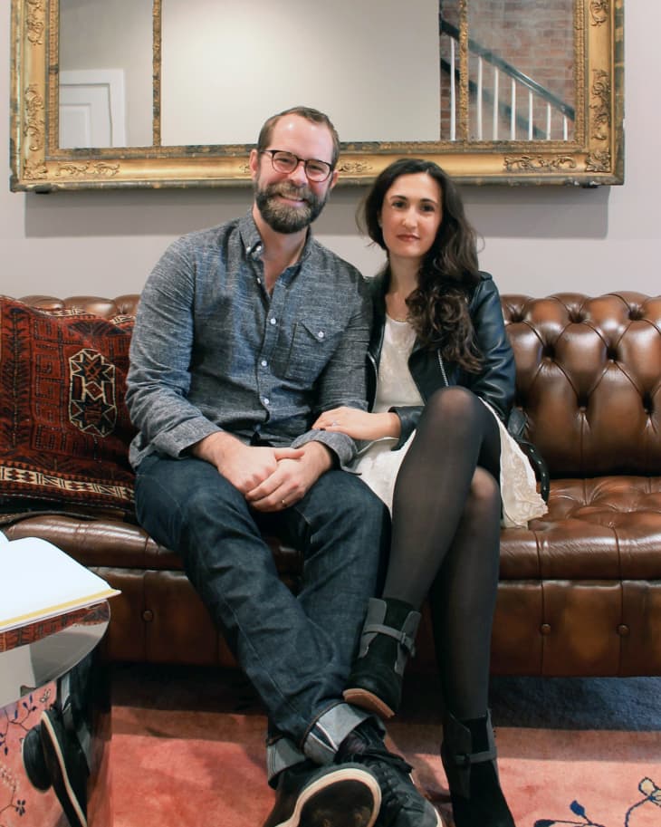 Couple sitting on a brown leather sofa with a large ornate mirror above them.