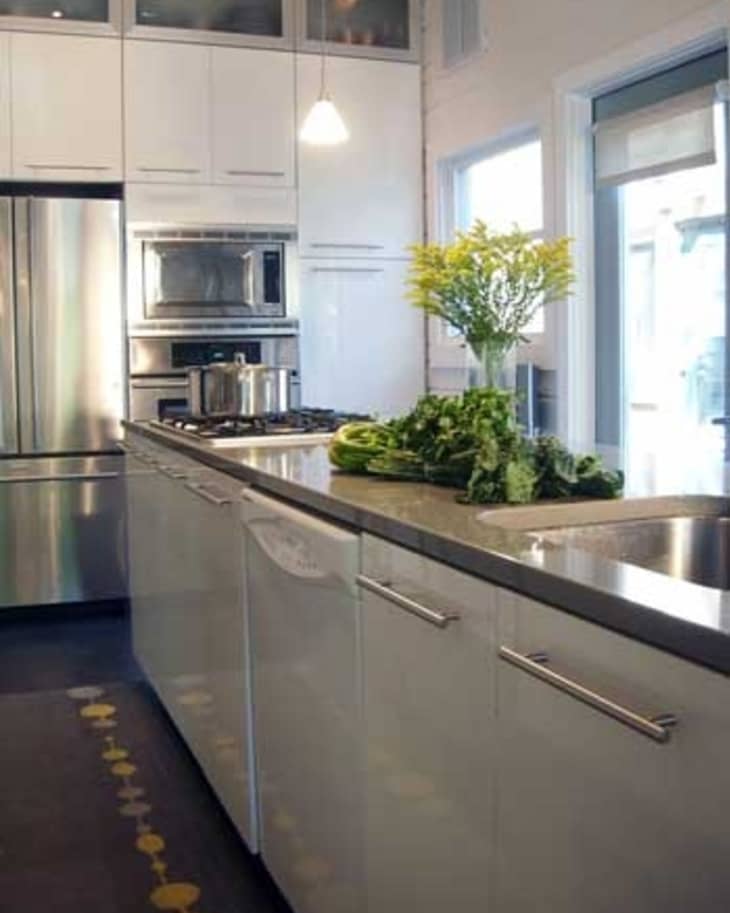 Modern kitchen with stainless steel appliances, white cabinets, and fresh greens on the countertop near a sink.
