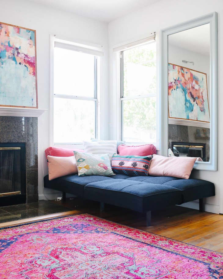 Navy futon with colorful pillows, abstract art, and a vibrant pink rug in a bright living room.