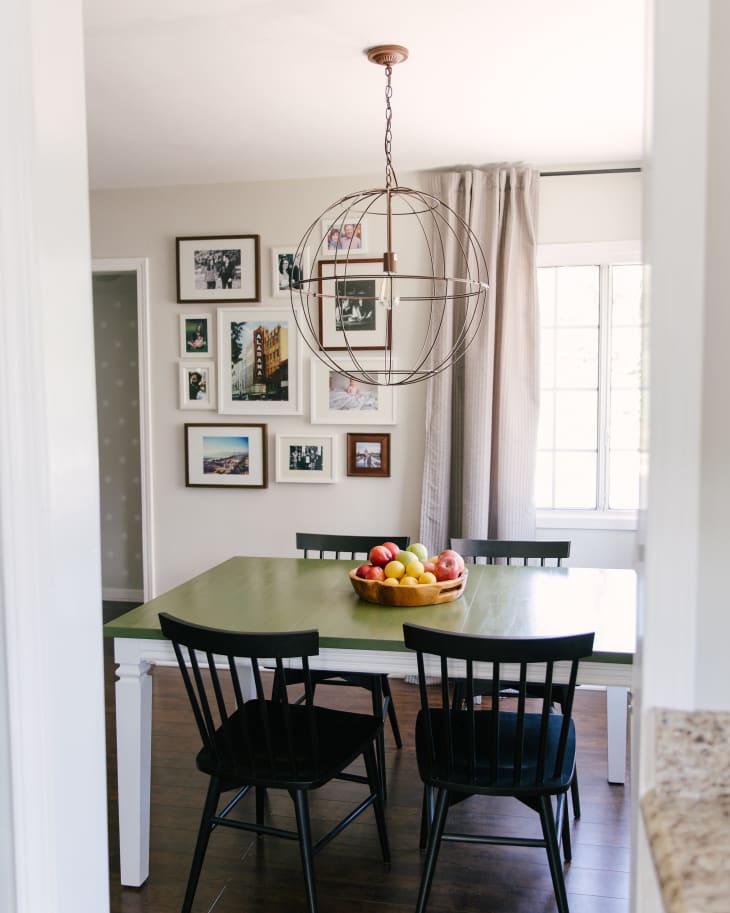 Dining room with green table, black chairs, fruit bowl centerpiece, gallery wall, and globe pendant light.