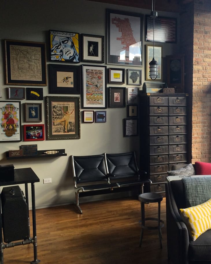 Gallery wall with eclectic framed art, black leather bench, industrial pendant light, and tall drawer cabinet in a cozy room.