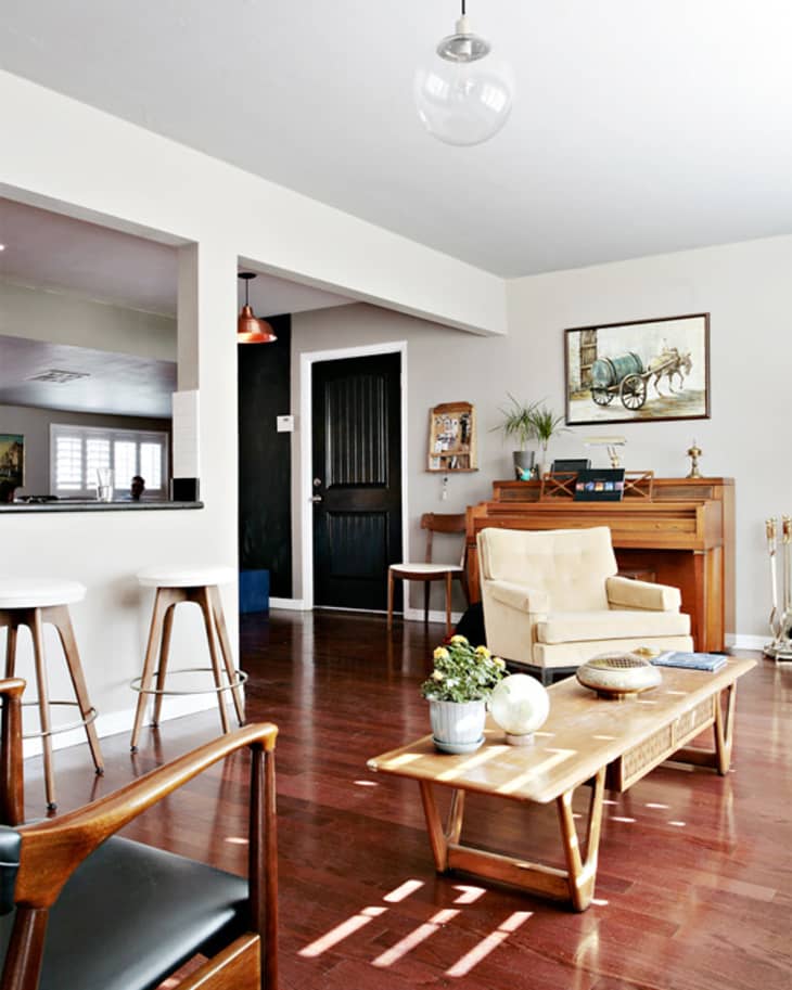 Living room with wooden floors, beige armchair, piano, coffee table, and wall art.