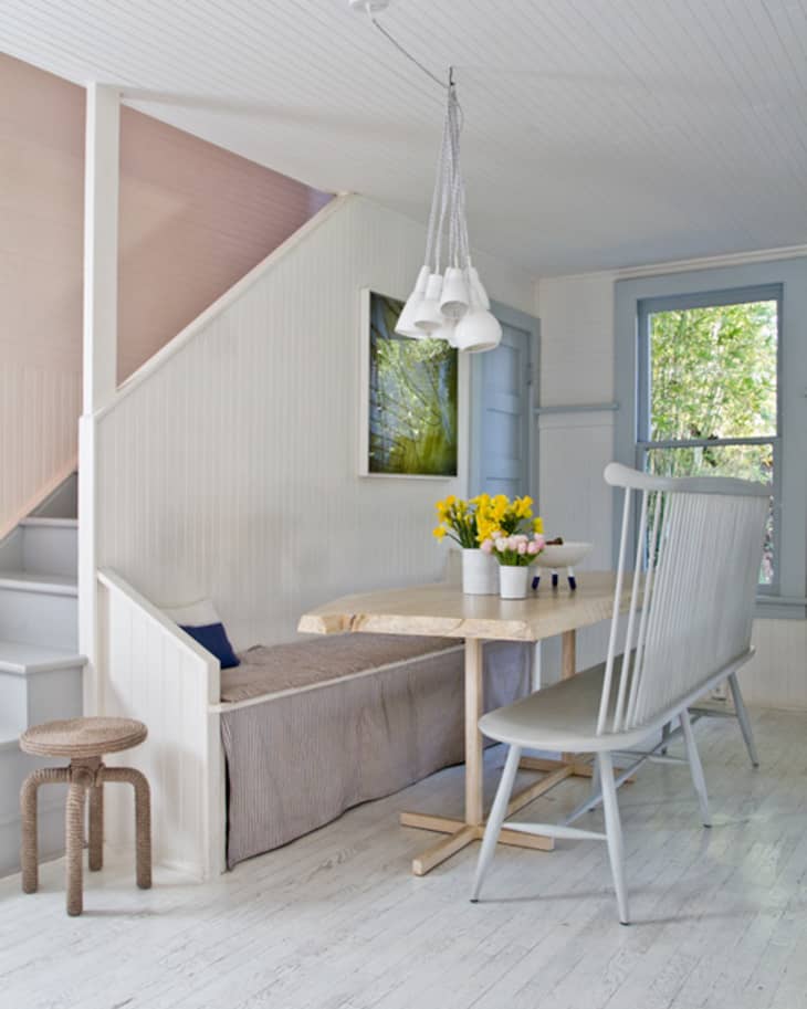 Cozy dining nook with a wooden table, bench seating, gray chairs, and a vase of yellow flowers under a modern pendant light.