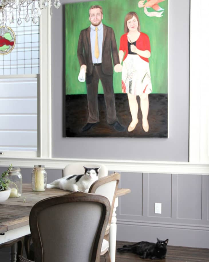 Dining room with a large painting, chandelier, wooden table, chairs, and two cats lounging.