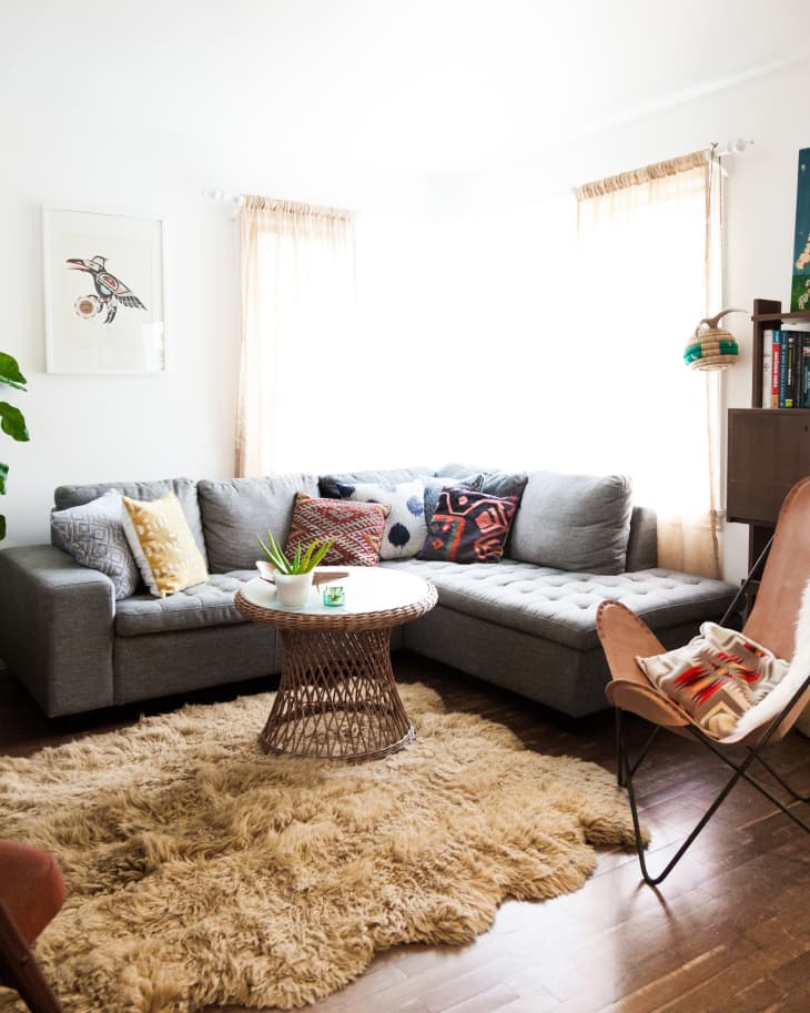 Cozy living room with a gray sectional sofa, patterned cushions, wicker coffee table, and a fluffy beige rug.