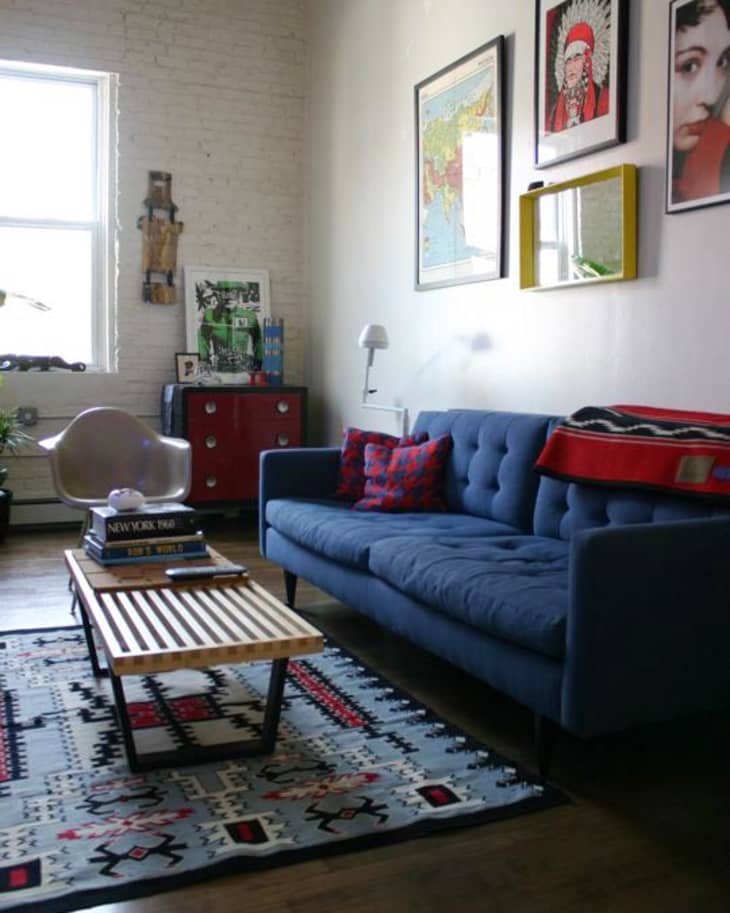 Living room with blue sofa, patterned rug, wooden coffee table, and eclectic wall art.