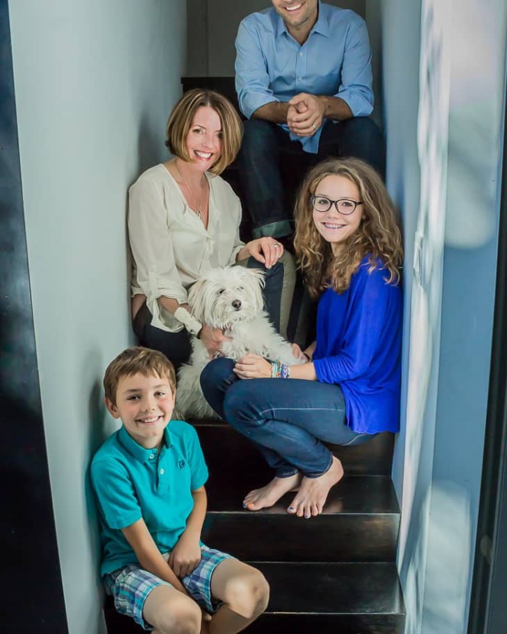 Family of four with a small white dog sitting on a staircase, smiling at the camera.