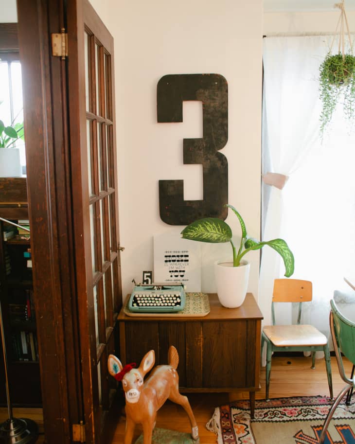 Eclectic room with a large number 3, vintage typewriter, potted plant, and a decorative deer statue on a colorful rug.