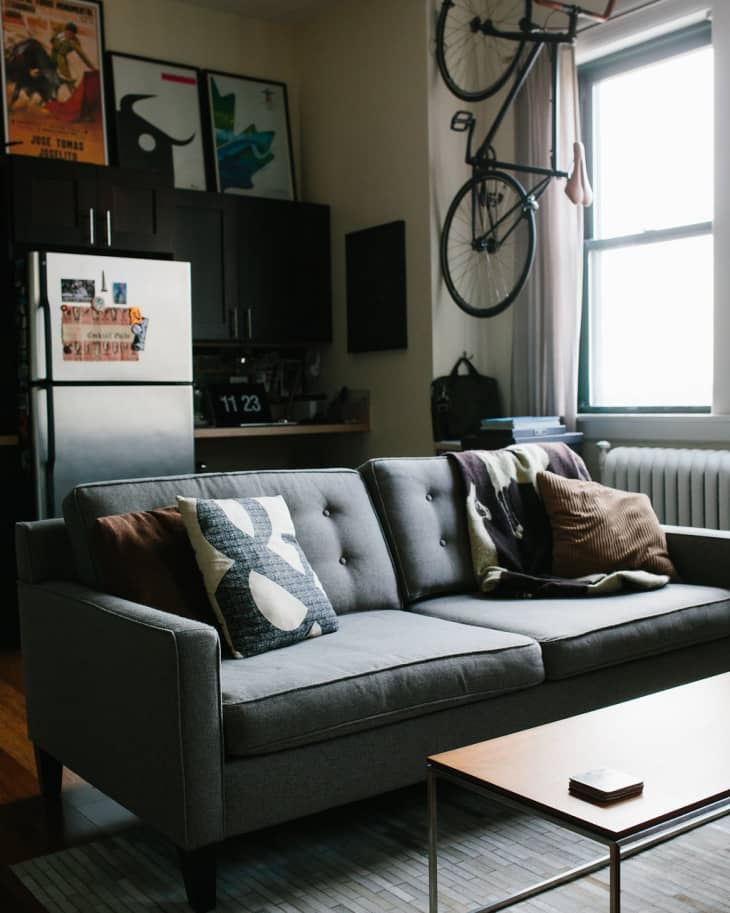Gray sofa with patterned pillows, wall-mounted bicycle, and framed art in a cozy living room with natural light.