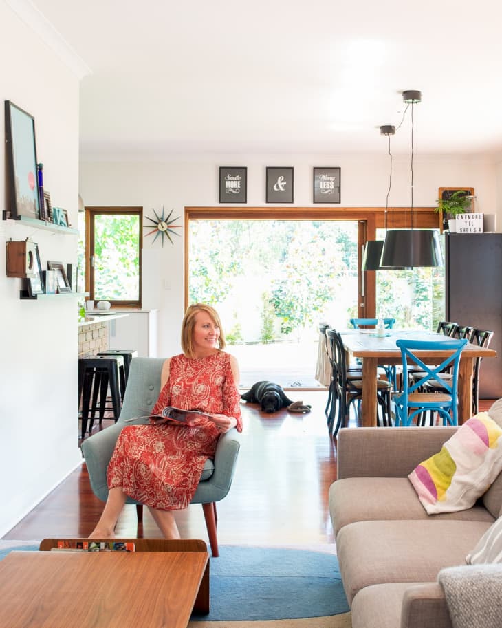 Woman in red dress sitting on a blue chair in a bright living room with modern decor and wooden dining table.