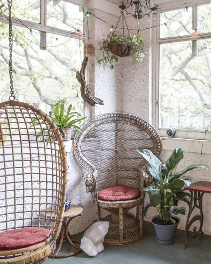 Wicker chairs with red cushions in a sunroom, surrounded by plants and string lights.