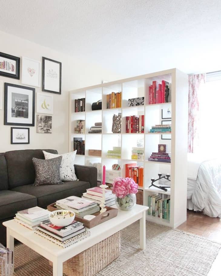 A large white bookshelf separating a bedroom from a living space in a studio apartment