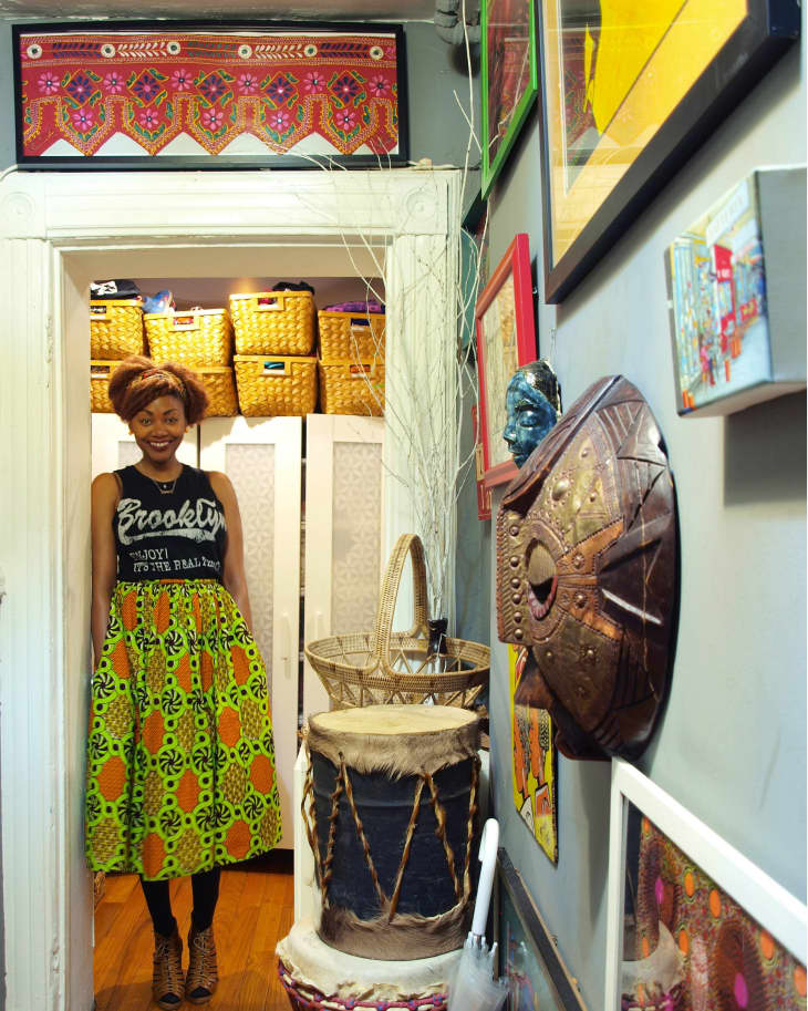 Woman in colorful skirt standing in hallway with baskets, drum, and wall art.