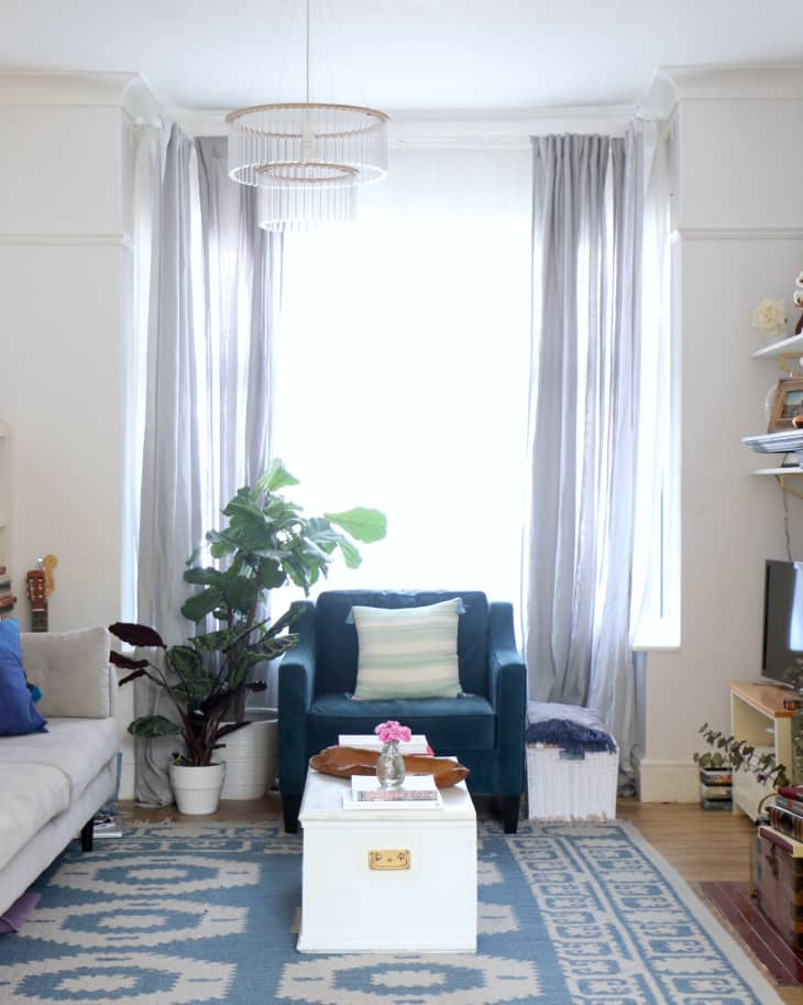 Living room with blue armchair, white coffee table, patterned rug, potted plant, and sheer curtains.