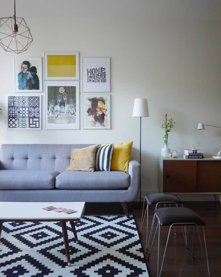 Living room with gray sofa, yellow and striped pillows, geometric rug, wall art, and a wooden sideboard with decor.
