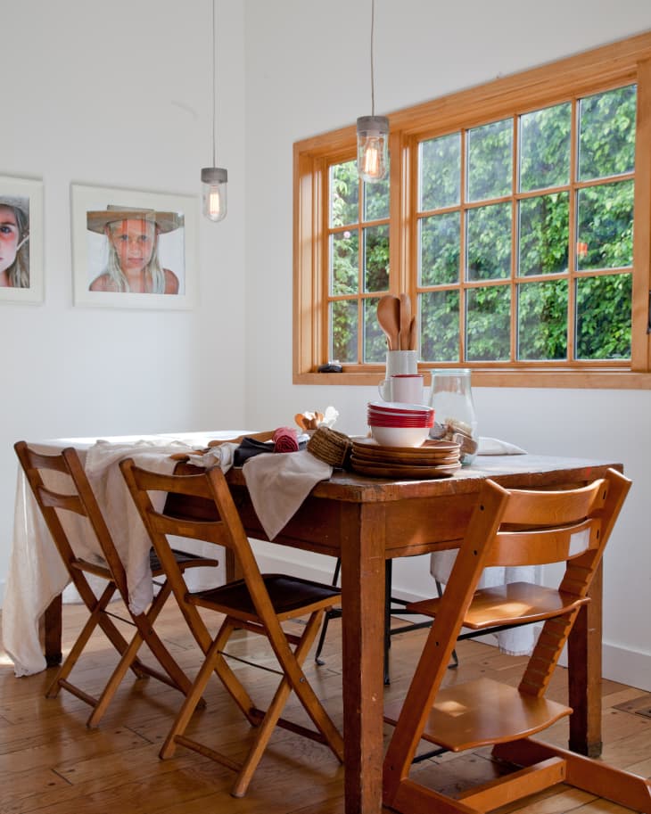 Dining room with wooden table, folding chairs, tableware, and large window with garden view.