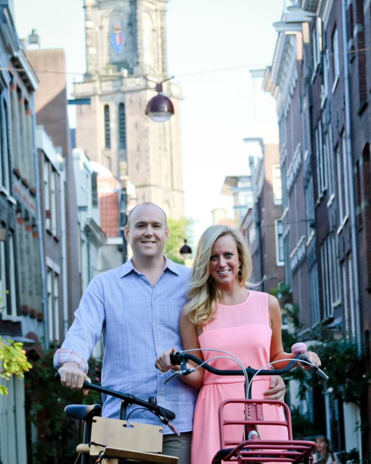 Couple with bicycles on a narrow street, with a tall clock tower in the background.
