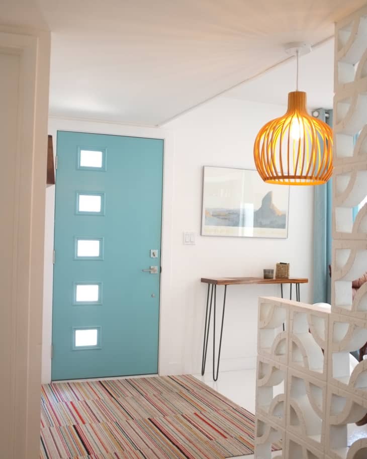 Entryway with a blue door, striped rug, wooden console table, and a hanging wicker light fixture.