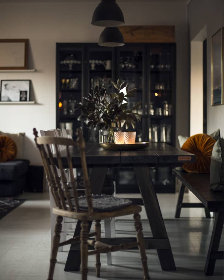Dining room with wooden table, chairs, pendant lights, and a cabinet. Candles and plant centerpiece on the table.