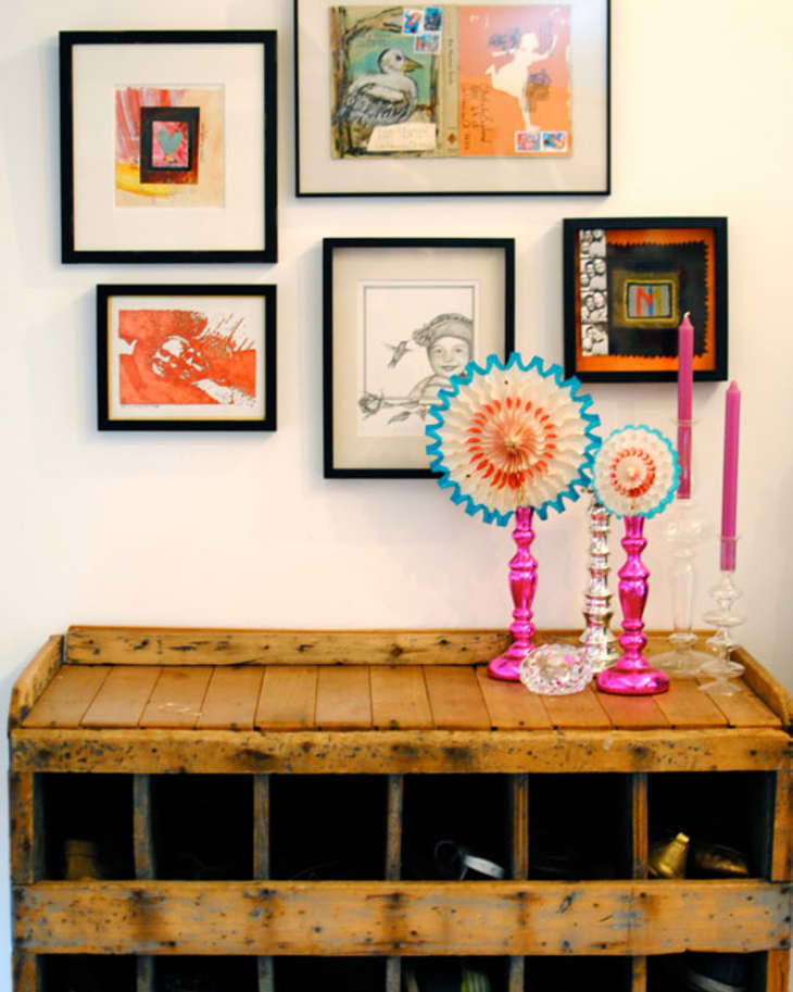 Wooden wine rack with framed art above, pink candlesticks, and decorative fans on top.