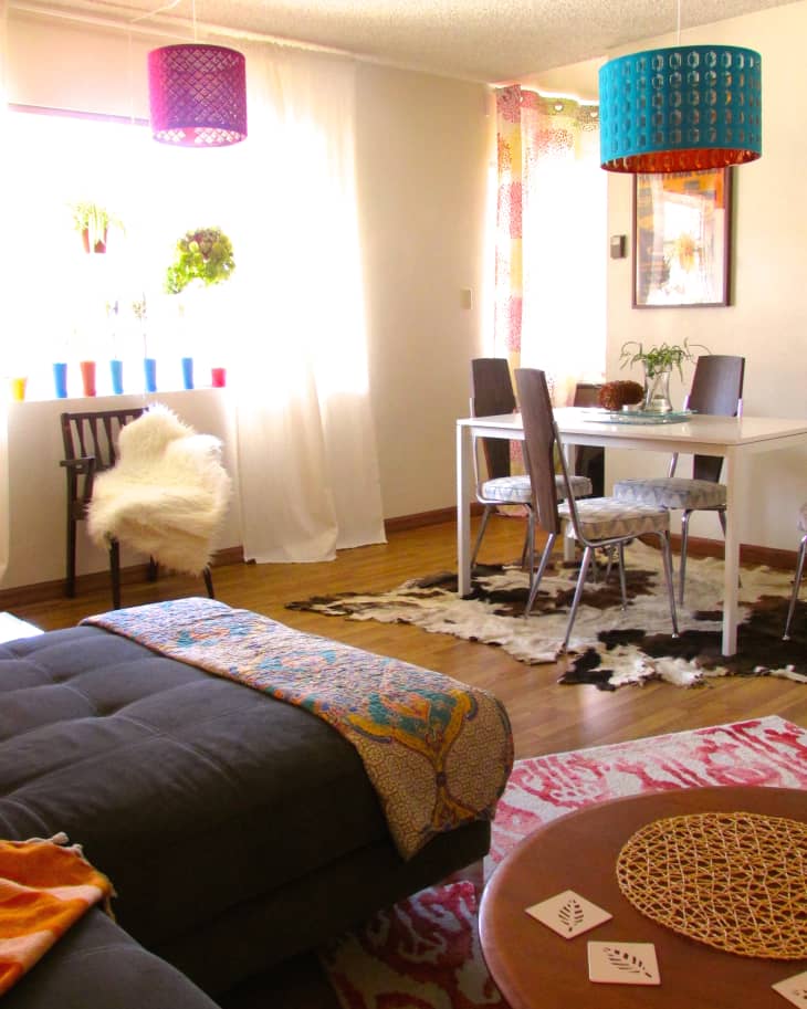 Living room with colorful pendant lights, a black sofa, patterned rugs, and a dining table with chairs on a cowhide rug.