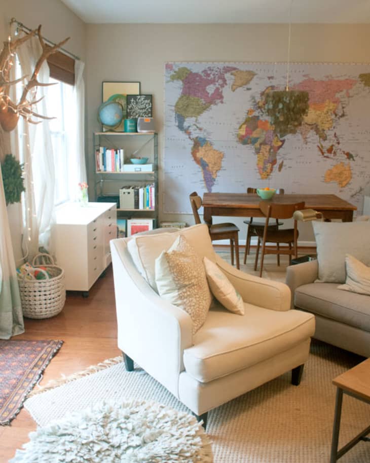 Cozy living room with a world map wall, beige armchair, bookshelf, and wooden dining table.