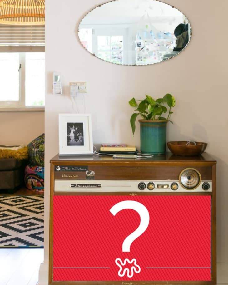Vintage stereo console with a potted plant, framed photo, and books, beneath an oval mirror in a cozy living room.