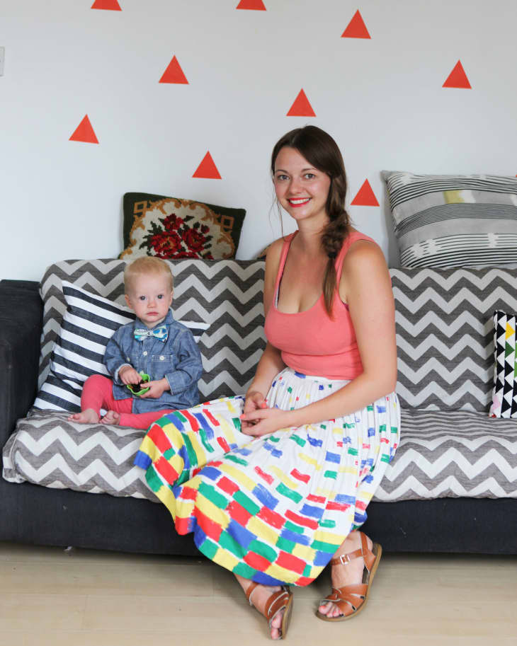 Woman in colorful skirt and child in bow tie sitting on chevron-patterned sofa with geometric wall decor.