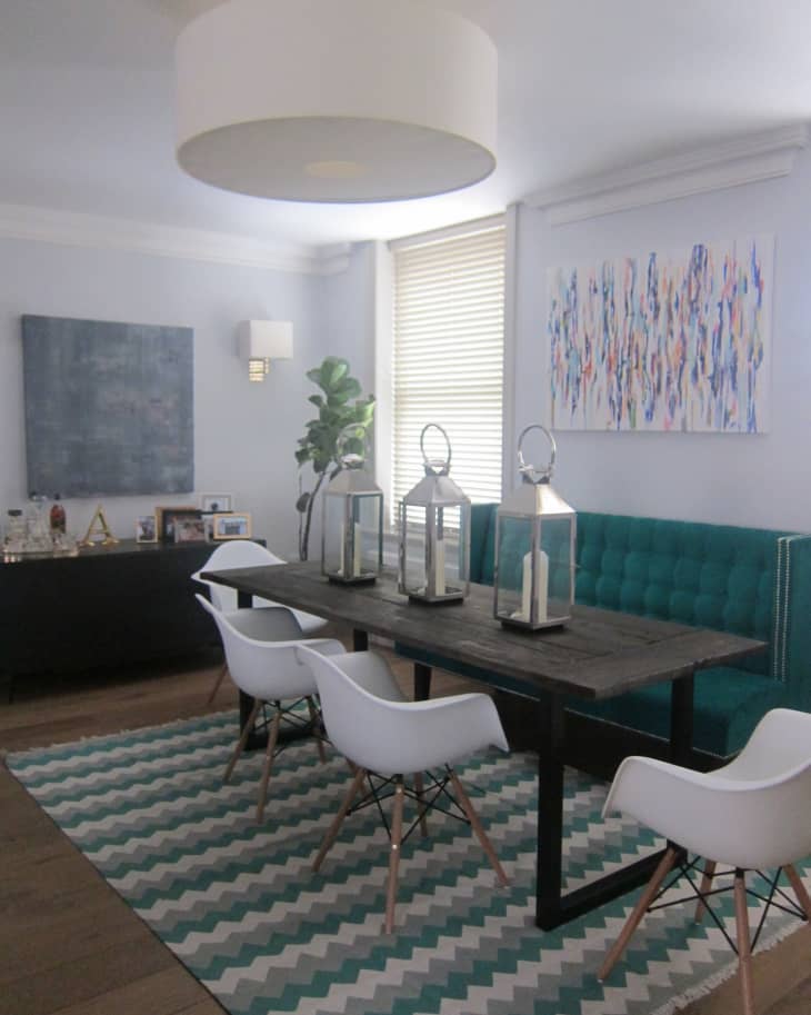Dining room with a dark wood table, white chairs, teal bench, zigzag rug, and abstract wall art.