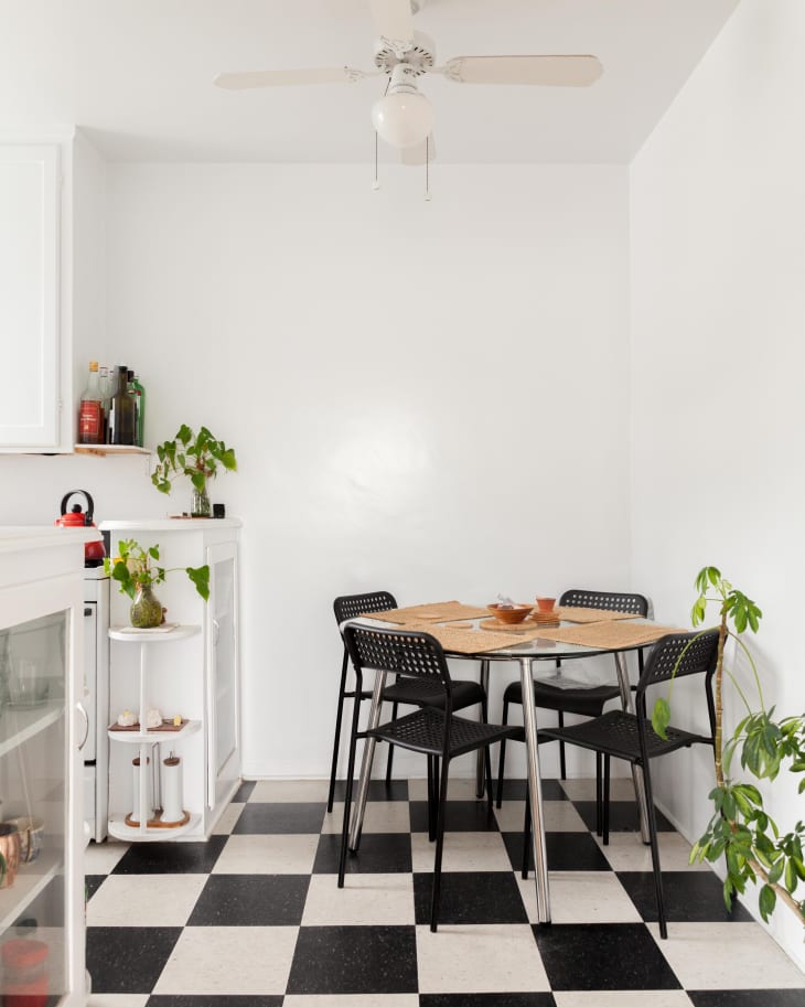 Small dining area with black and white checkered floor, round table, four black chairs, and potted plants.