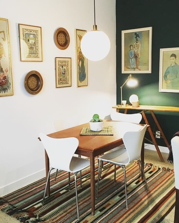 Dining room with wooden table, white chairs, patterned rug, wall art, and a globe pendant light.