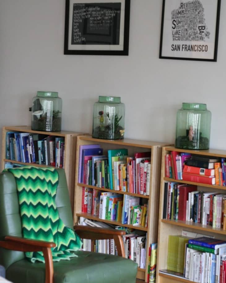 Green armchair with a zigzag throw, bookshelves filled with colorful books, and decorative jars on top.