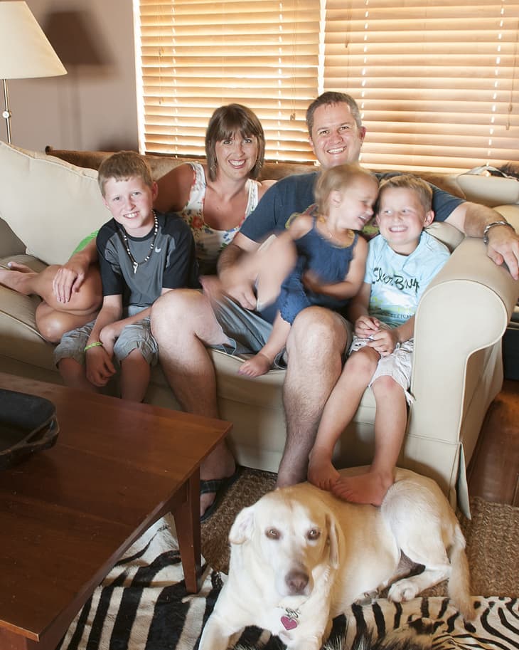Family sitting on a beige sofa with a dog on a zebra-patterned rug in a cozy living room.