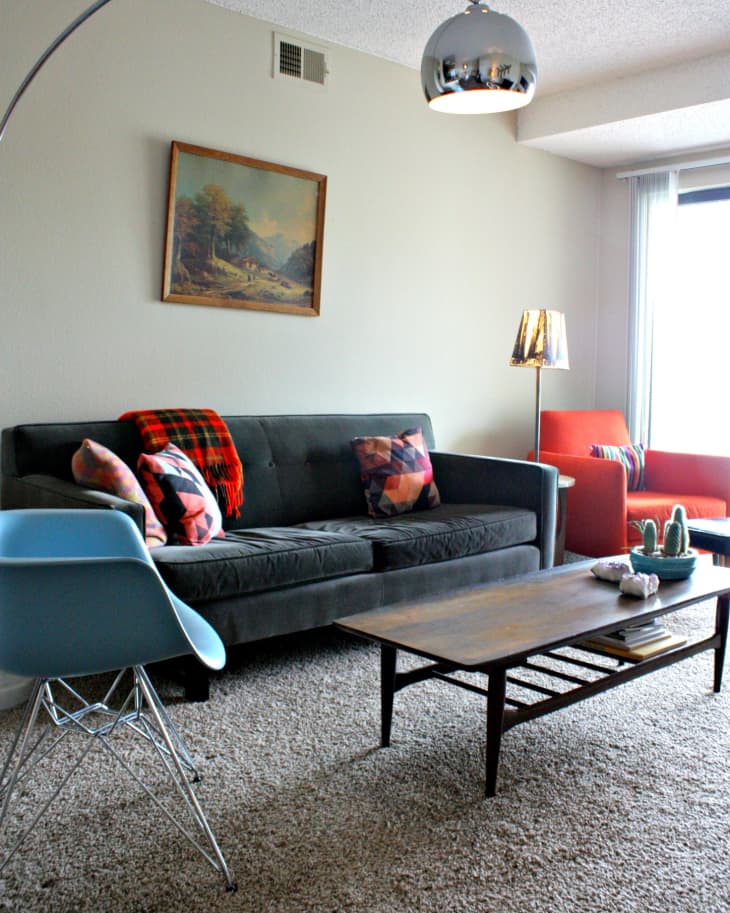 Living room with gray sofa, colorful pillows, plaid throw, blue chair, wooden coffee table, and arc floor lamp.