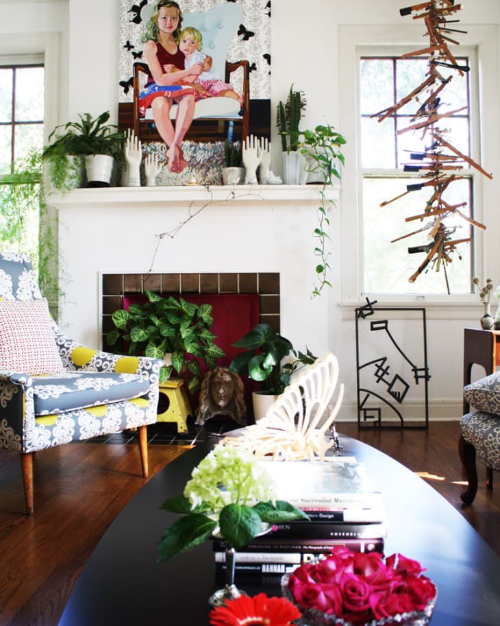 Living room with eclectic decor, colorful armchair, abstract art, plants, and a black coffee table with flowers and books.